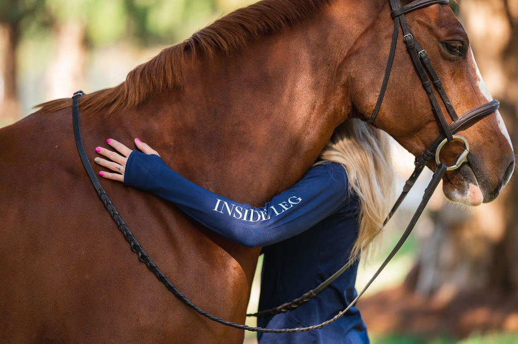 Woman hugging horse around its neck. "Inside Leg" printed along sleeve of her shirt.
